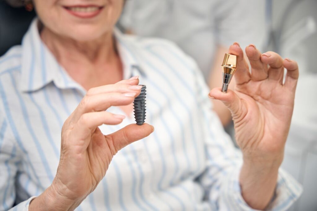 Dental professional holding an All-On-Four implant component and a traditional dental implant for comparison