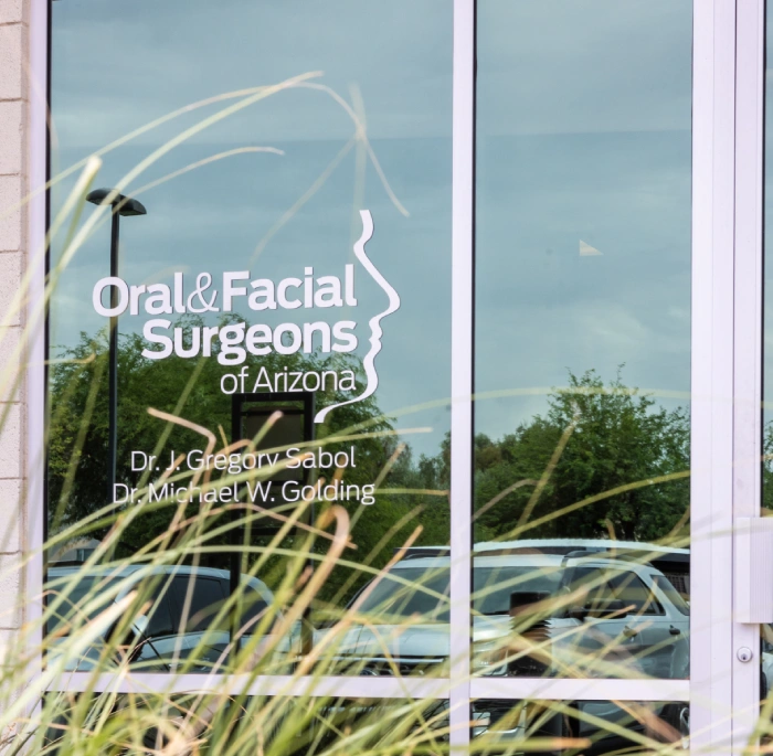 Glass door entrance displaying Oral & Facial Surgeons of Arizona logo with outdoor landscape visible through window.