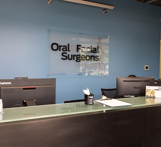 Modern dental office reception area with "Oral Facial Surgeons" signage on blue wall.