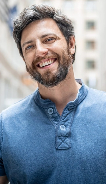 Smiling man in blue shirt, outdoor urban setting, professional headshot for dental practice.