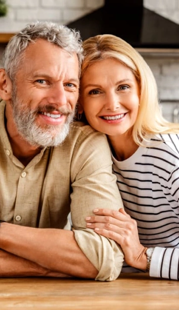 Smiling mature couple posing together at kitchen counter in casual home setting.