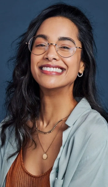 Woman with glasses smiling at camera against blue background, professional headshot.