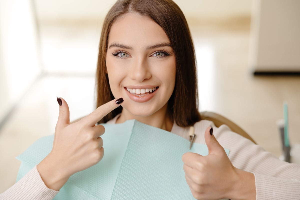 Happy patient pointing to her healthy smile after dental treatment.