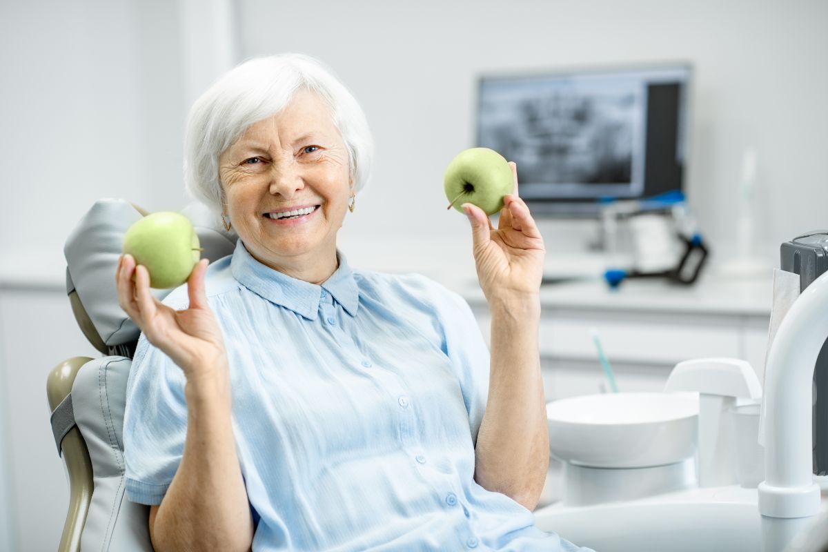 Senior patient holding green apples at dental office in Phoenix, AZ after dental implant treatment.