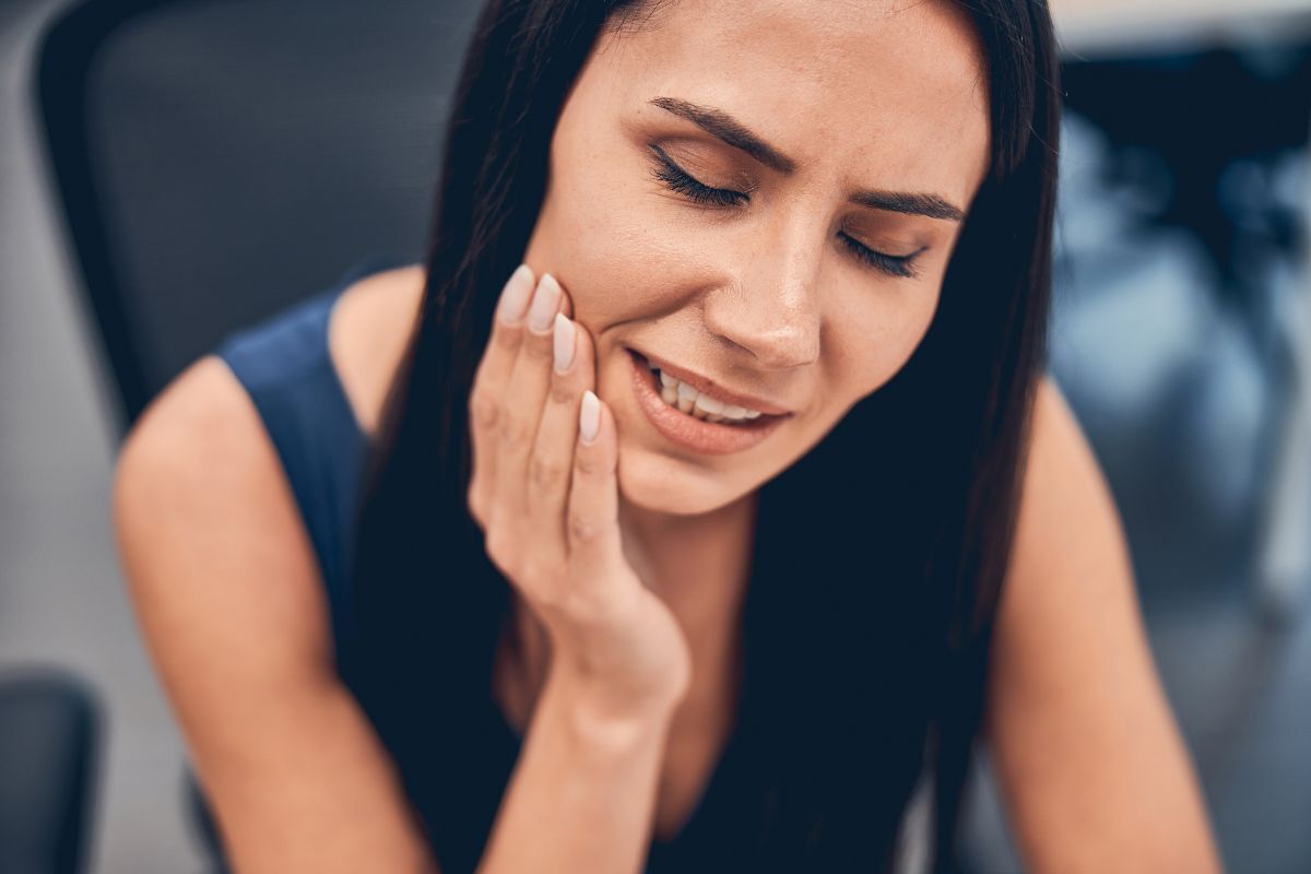 Woman experiencing jaw or tooth pain, holding her cheek with a concerned expression.